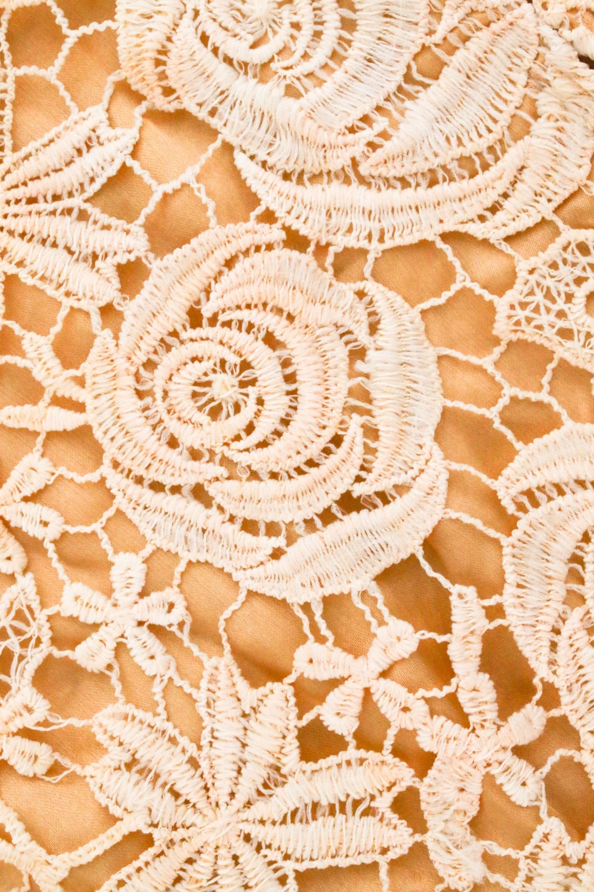White floral lace with raised outlines on a warm beige fabric.
