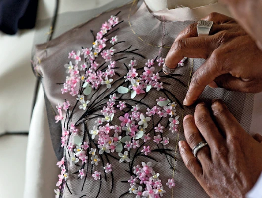 Hands adding pink and white floral embellishments to sheer fabric.