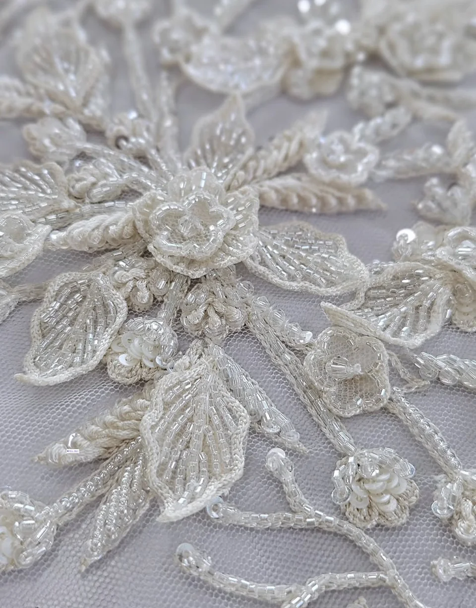 White flowers and leaves outlined with fine reflective details on an open mesh ground.